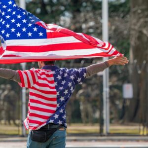 Man wearing American flag shirt and holding flag in Washington DC, symbolizing patriotism.
