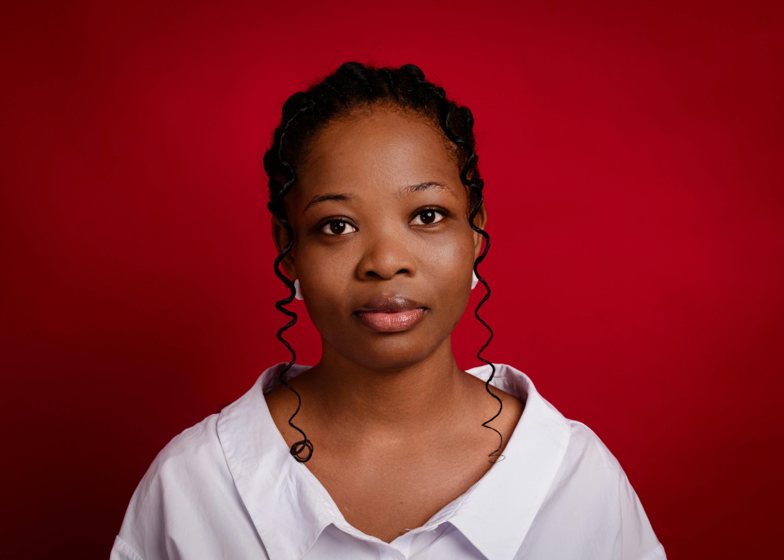 Studio portrait of a young woman with curly hair posing against a vibrant red background.