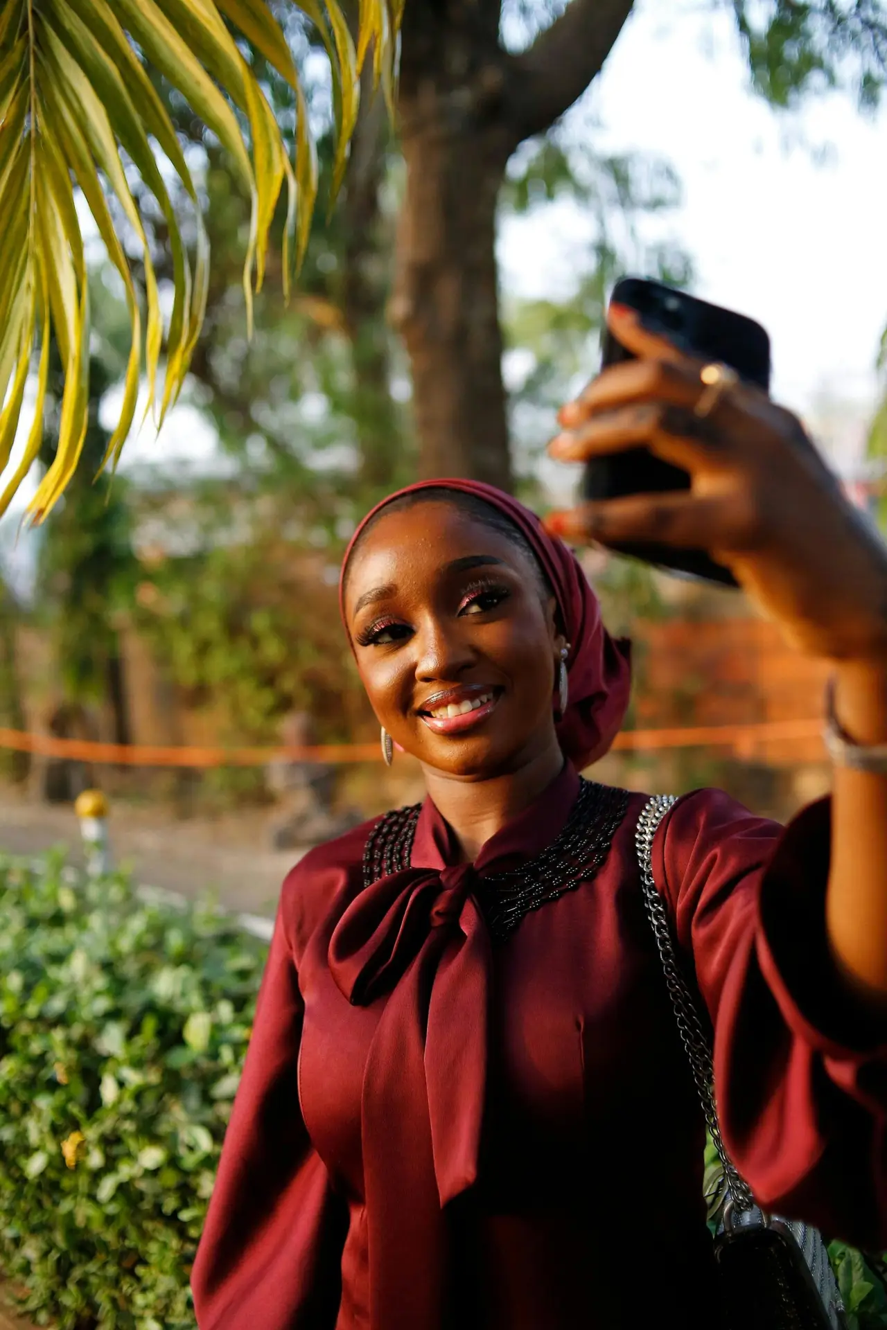 A young woman in traditional attire takes a selfie outdoors in Abuja, Nigeria.