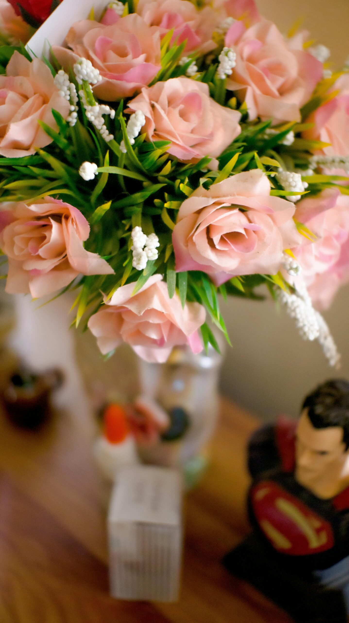 From above view of fresh blooming bouquet of pink roses in vintage vase placed on wooden table among household items in daylight