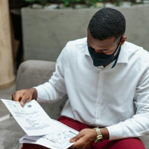 Adult man in a white shirt sits indoors, attentively examining documents while wearing a face mask.