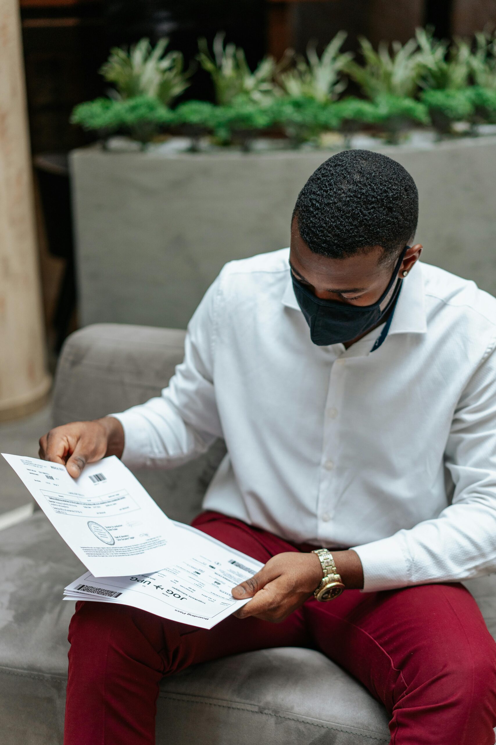 Adult man in a white shirt sits indoors, attentively examining documents while wearing a face mask.