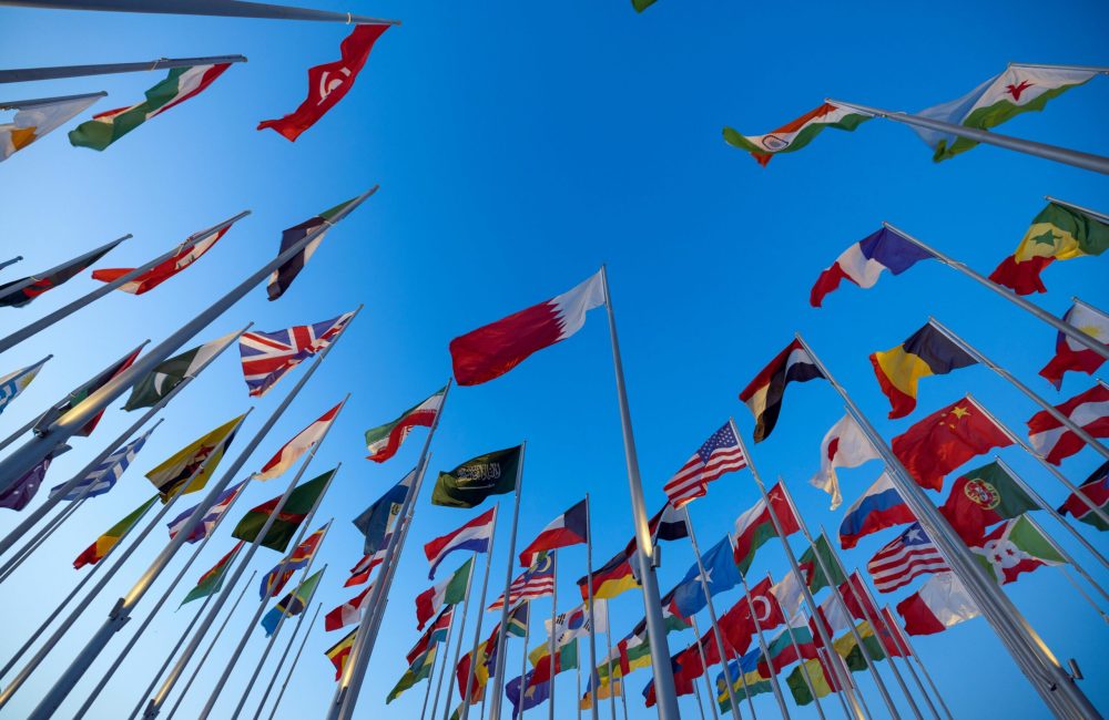 International flags waving against a clear blue sky in Doha, Qatar, symbolizing unity and diversity.